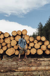 Männlicher Wanderer steht auf einem Baumstamm gegen einen Holzstapel im Wald - BOYF01552
