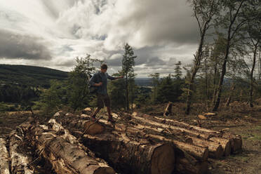 Male hiker walking on logs against cloudy sky in forest - BOYF01573