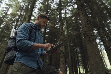 Mann überprüft GPS über digitales Tablet, während er im Wald vor Bäumen steht - BOYF01576