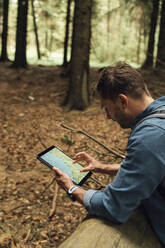 Männlicher Wanderer, der im Wald stehend eine Karte auf einem digitalen Tablet analysiert - BOYF01578