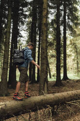 Männlicher Wanderer mit Rucksack, der auf einem Baumstamm gegen Bäume in einem Waldgebiet läuft - BOYF01591