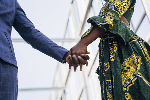 Young woman in traditional dress holding man's hand while standing in building - MPPF01073