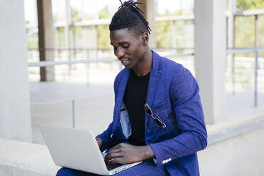 Young man using laptop while sitting on retaining wall - MPPF01074