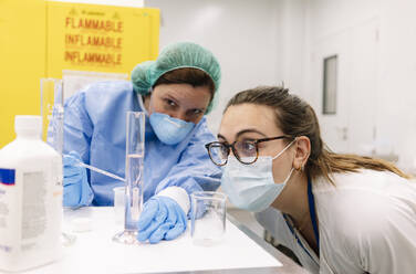 Female pharmacists examining chemical in graduated cylinder at laboratory - DGOF01264