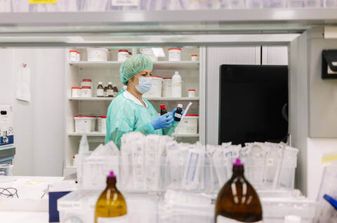 Female pharmacist holding bottles while standing by shelf in hospital stock photo