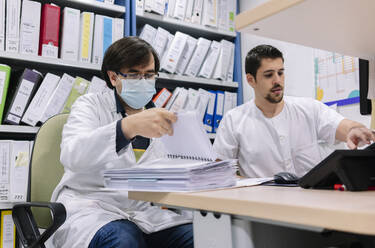 Männliche Ärzte erledigen Papierkram auf dem Schreibtisch in der Apotheke eines Krankenhauses - DGOF01268