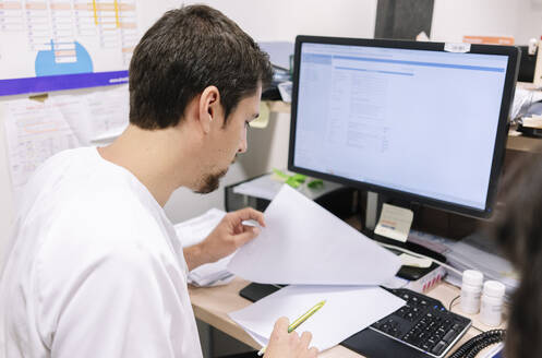 Male doctor examining medical record while sitting at desk in hospital - DGOF01270