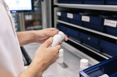 Close-up of male doctor holding medicine bottle at table in pharmacy - DGOF01273