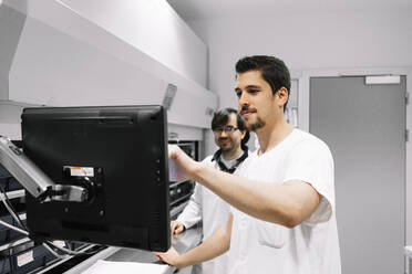 Männliche Ärzte, die einen Computer benutzen, während sie in der Apotheke eines Krankenhauses stehen - DGOF01280