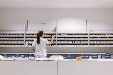 Female pharmacist arranging medicines on shelves in hospital - DGOF01293