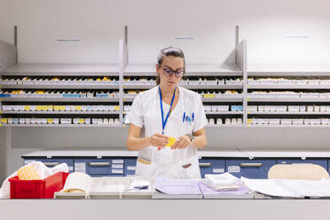 Female pharmacist packing medicines on table while standing in storage room - DGOF01294