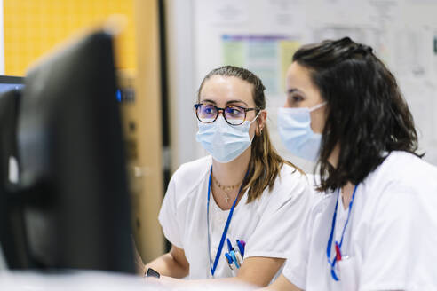 Nahaufnahme von Ärztinnen mit Masken bei der Arbeit am Computer im Krankenhaus - DGOF01308