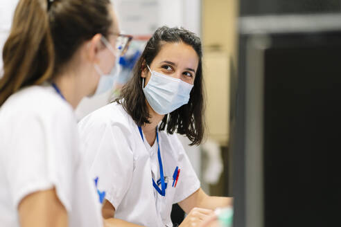 Close-up of female doctors wearing masks discussing while sitting in hospital - DGOF01309