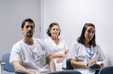 Ärzte hören in einer Sitzung zu, während sie im Krankenhaus an der Wand sitzen - DGOF01317