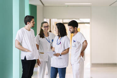 Ärzte diskutieren über ein digitales Tablet, während sie auf dem Flur eines Krankenhauses stehen - DGOF01322