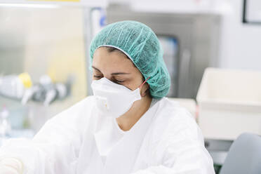 Nahaufnahme einer Apothekerin mit chirurgischer Maske und Kappe bei der Arbeit im Labor - DGOF01338
