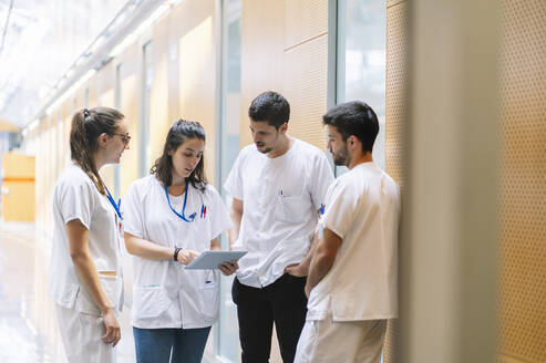 Male and female pharmacists discussing over digital tablet while standing in hospital - DGOF01346