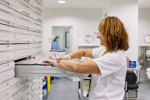 Female doctor arranging medicines in drawer at storage room - DGOF01371