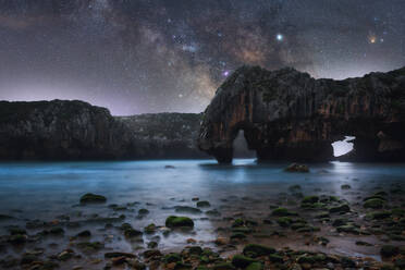 Amazing scenery of sea coast with calm water and rocky cliffs with caves under dark sky with Milky Way - ADSF15051