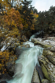 Draufsicht auf eine erstaunliche Naturlandschaft mit einem reißenden, flachen Fluss, der zwischen Felsbrocken in bergigem Gelände mit Wald an einem bewölkten Herbsttag fließt - ADSF15057