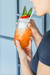 Gesichtslose Frau nippt an einem kühlen Cocktail mit Strohhalm aus einem Glas in Form einer Ananas - ADSF15096