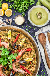 Top view of pan with arroz marinero garnished with lemon and chili peppers with parsley served on table with ingredients - ADSF15099