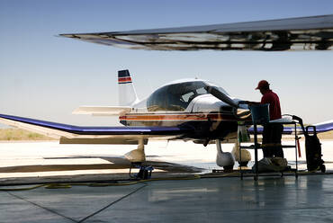 Seitenansicht eines männlichen Angestellten in Uniform, der ein Düsenflugzeug reinigt, während er an einem sonnigen Tag auf einem Flugplatz steht - ADSF15110