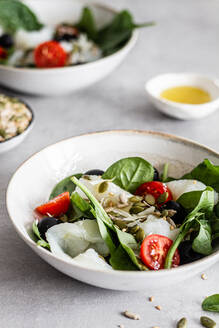 Von oben Schalen mit köstlichem Salat aus Fisch und grünem Spinat mit gehackten Kirschtomaten und schwarzen Oliven, garniert mit Kernen - ADSF15133