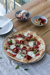 From above of delicious golden quiche with crunchy puff pastry and burrata cheese with tomato slices on top decorated with pine nuts near bowl with bacon and champignon - ADSF15143