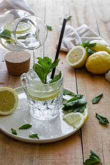 Kaltes Erfrischungsgetränk mit Sodawasser und Zitrone, garniert mit frischen Minzblättern, serviert in einem Glasbecher mit Strohhalm auf einem Holztisch - ADSF15145