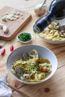 Unrecognizable cook pouring olive oil in bowl with spaghetti and clams placed on wooden table in restaurant - ADSF15146