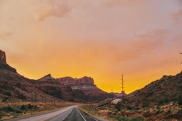 Goldener Sonnenuntergang über Gewitterwolken entlang eines leeren Highways in Moab, Utah. - CAVF88750