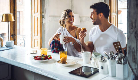 Glückliches junges Paar sitzt am Tisch und frühstückt zu Hause, lizenzfreies Stockfoto