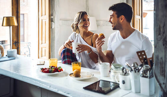 Glückliches junges Paar sitzt am Tisch und frühstückt zu Hause - EHF00896