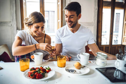 Happy young couple sitting at table and having breakfast at home stock photo