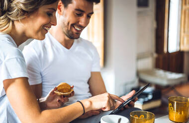 Junges Paar schaut beim Frühstück zu Hause auf ein Tablet - EHF00905