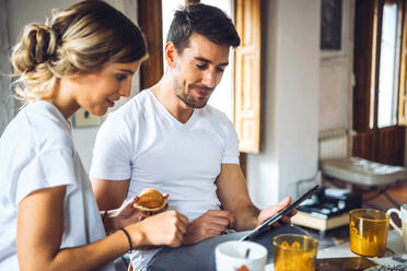 Junges Paar schaut beim Frühstück zu Hause auf ein Tablet - EHF00906