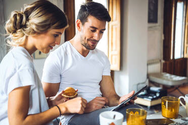 Young couple watching tablet while having breakfast at home - EHF00906