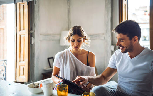Junges Paar schaut beim Frühstück zu Hause auf ein Tablet - EHF00907