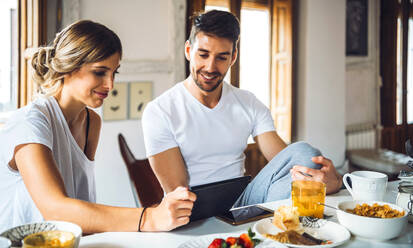 Junges Paar schaut beim Frühstück zu Hause auf ein Tablet - EHF00908