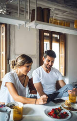 Young couple watching tablet while having breakfast at home - EHF00909