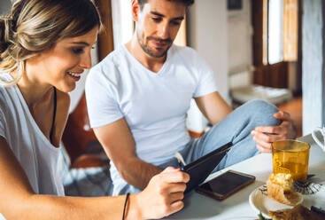 Young couple watching tablet while having breakfast at home - EHF00910