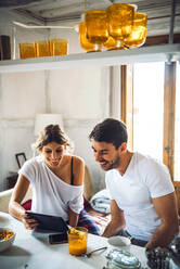 Happy young couple watching tablet while having breakfast at home - EHF00913