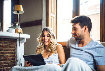 Junges Paar kuschelt auf der Couch zu Hause und schaut Tablet - EHF00916