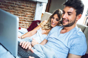 Glückliches junges Paar sitzt zu Hause auf der Couch und schaut auf den Laptop - EHF00921