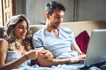 Young couple sitting on couch at home with credit card and laptop - EHF00922