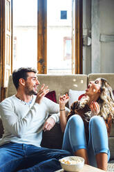 Fröhliches junges Paar sitzt zu Hause und spielt mit Popcorn - EHF00926