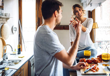 Junger Mann bereitet Essen zu und gestikuliert mit Freundin in der Küche zu Hause - EHF00931