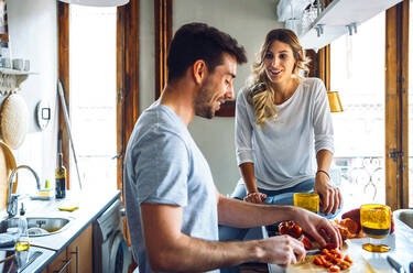 Young man preparing food and talking with girlfriend in kitchen at home - EHF00932