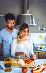 Young woman chopping bell pepper while cooking dinner with man watching - EHF00938